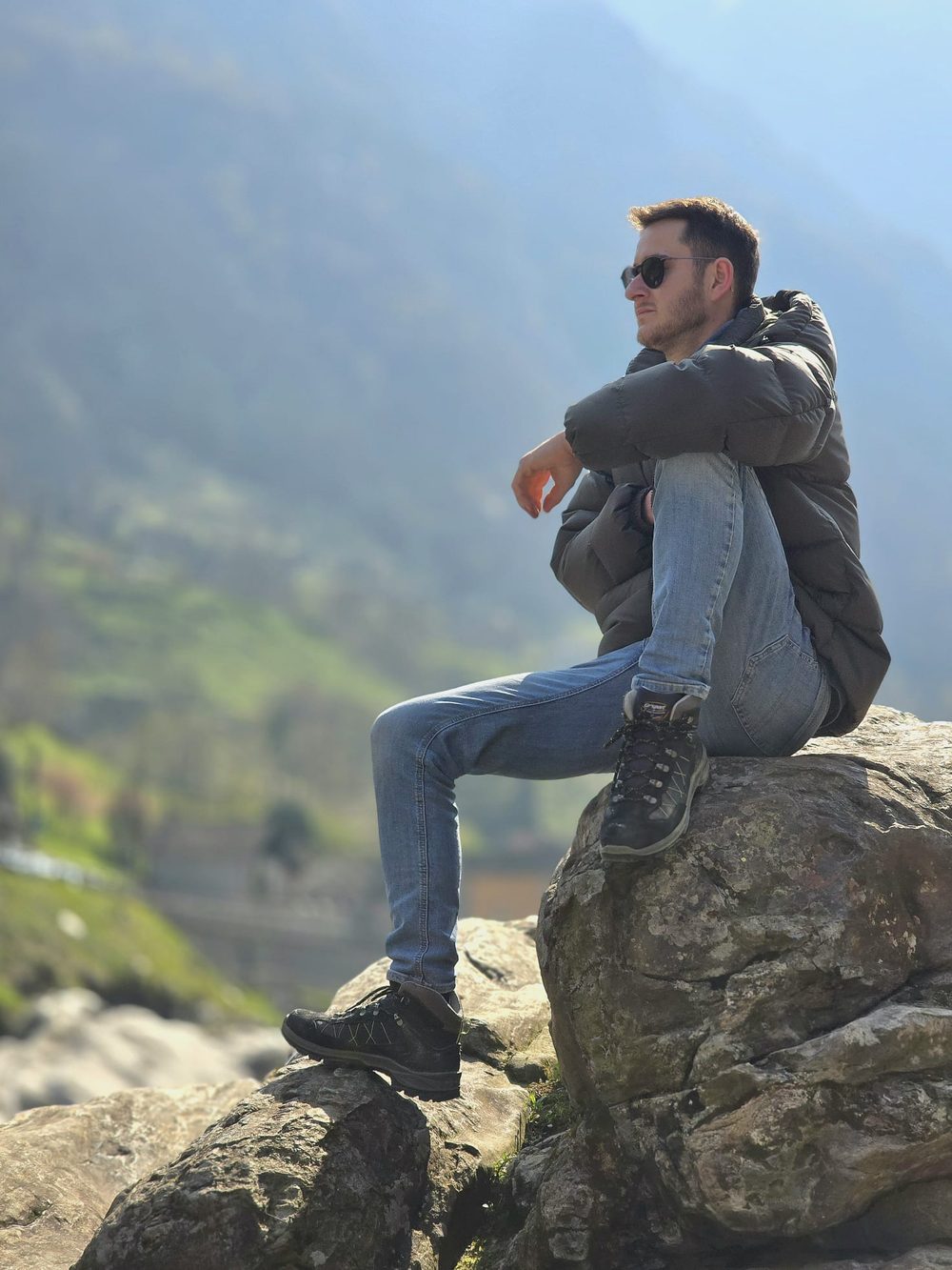 Person sitzt ruhig auf einem Felsen und blickt über das Tal
